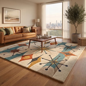 May include: A rectangular area rug featuring a cream-colored background with a repeating pattern of teal, orange, and dark gray starburst and diamond shapes. The rug has a textured pile and is positioned on a wooden floor in a living room setting.