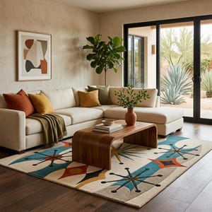 May include: A large area rug featuring a cream background with a repeating pattern of teal, orange, and black starburst and diamond shapes. The rug is positioned on a dark wood floor in front of a cream-coloured sectional sofa with various throw pillows.