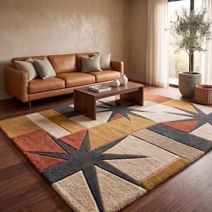 May include: A rectangular area rug featuring a geometric pattern with starburst motifs in shades of burnt orange, mustard yellow, cream, and charcoal gray. The rug has a textured, tufted pile construction and covers a dark wood floor in a living room.