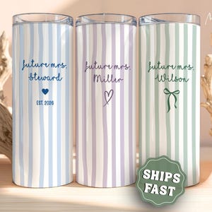 May include: Three cylindrical tumblers with clear lids, each featuring vertical stripes in light blue, lavender, and sage green. Each tumbler displays the text future mrs. followed by a surname, a small icon, and a date or symbol.