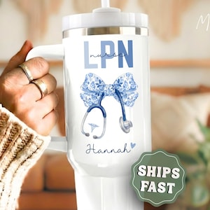 May include: A white stainless steel tumbler with a handle and lid, featuring the text LPN and nurse in blue, a blue floral patterned bow, a stethoscope graphic with a medical caduceus symbol, and the name Hannah with a small blue heart.