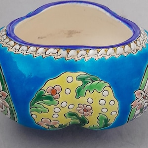 Peut inclure: Un bol en céramique arrondi présentant un extérieur bleu vif avec un panneau central jaune orné de points blancs, de feuilles vertes et de petites fleurs roses. Le bord est accentué par une bordure bleue et un motif festonné blanc.