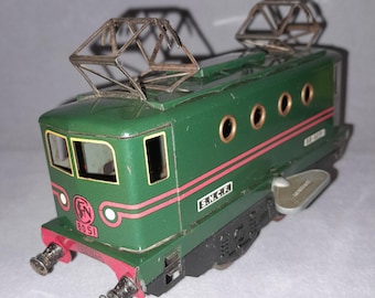 May include: A vintage green toy electric locomotive featuring two metal pantographs on top, red horizontal stripes, and the text S.N.C.F. on the side. The front displays the number 8051 in red, with two silver buffers at the base and four circular windows.