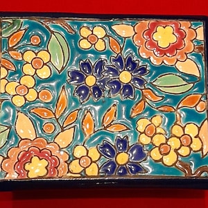 May include: A rectangular ceramic box with a glossy finish featuring a vibrant floral pattern. The design includes yellow, orange, and dark blue flowers with green leaves set against a bright turquoise background, framed by a solid dark blue border.