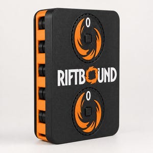 Op de afbeelding: Een zwart en oranje rechthoekig spel-telapparaat met de tekst RIFTBOUND in het wit gedrukt. De voorzijde bevat twee ronde draaischijven met oranje vlamachtige afbeeldingen en een nul-indicator. De zijkant toont een reeks zwarte ronde knoppen.