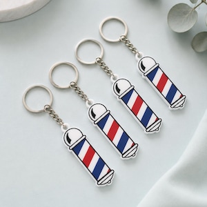 Pode incluir: Quatro porta-chaves idênticos com um design clássico de poste de barbeiro. Cada porta-chaves tem um anel e uma corrente de metal prateado fixados a um pendente retangular de acrílico com riscas diagonais vermelhas, brancas e azuis.