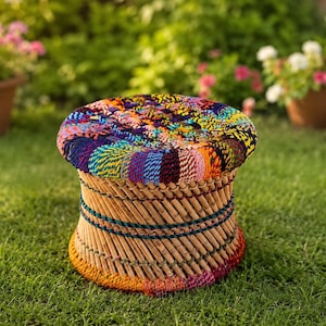 Peut inclure: Un tabouret rond doté d'une assise recouverte d'un tissu tissé multicolore. La base est constituée de bâtons en bois brun clair disposés en diagonale, agrémentés de bandes horizontales de corde colorée sur les parties supérieure et inférieure.