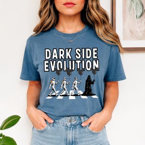 May include: Blue t-shirt with the text "DARK SIDE EVOLUTION" above a graphic of characters from Star Wars crossing a crosswalk. The characters include Stormtroopers and Darth Vader holding Mickey Mouse balloons.