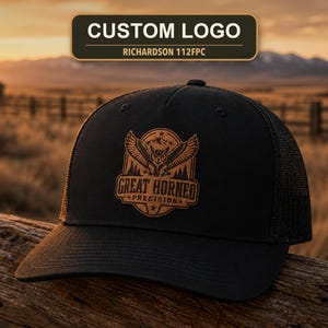 May include: A black trucker hat featuring a brown leather patch on the front. The patch displays an engraved graphic of an owl with spread wings above the text "GREAT HORNED PRECISION" and a mountain landscape. The hat has a mesh back panel.