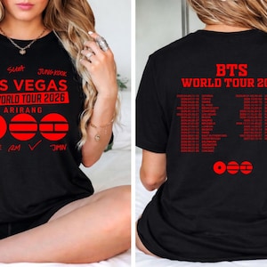 Puede incluir: Camiseta negra con texto y gráficos rojos. La parte delantera dice "LAS VEGAS BTS WORLD TOUR 2026 ARIRANG" con nombres de miembros de la banda y símbolos. La parte trasera muestra "BTS WORLD TOUR 2026" y una lista de fechas de gira.