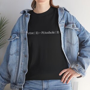 May include: Black crew neck t-shirt with the text "Artist | E > P(Asshole | E)" in white. The shirt is worn with a blue denim jacket and blue jeans.