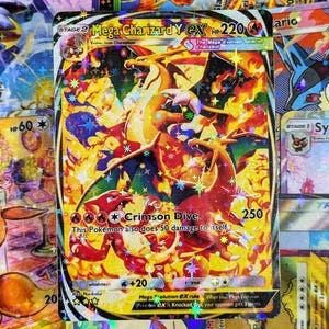 May include: A holographic Mega Charizard Y EX Pokémon card. The card features a fiery orange and yellow Charizard with the text "Crimson Dive" and "250" on the card. Other Pokémon cards are visible in the background.