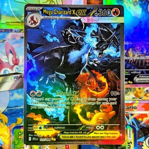 Puede incluir: Una carta Pokémon Mega Charizard X EX holográfica. La carta presenta una ilustración detallada de Charizard en tonos azules y negros, con llamas. El texto de la carta incluye "Inferno X" y "Mega Evolution EX rule".