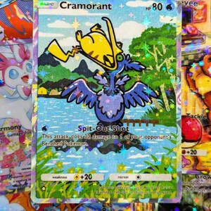 May include: A holographic Pokémon trading card featuring Cramorant, a blue bird-like creature with a yellow object in its beak. The card has a scenic background with text that reads "Spit-Out Shot". The card also has the text "HP 80".