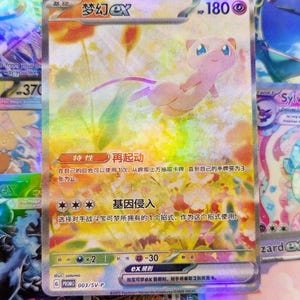 May include: A holographic Pokémon trading card featuring Mew. The card has a pink Mew illustration with a purple tail and a yellow and orange background. The card has Japanese text and is a promo card.