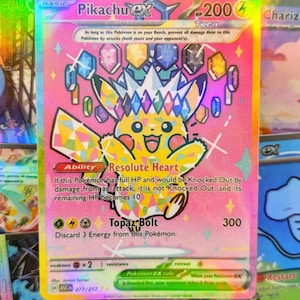 May include: A holographic Pikachu EX Pokémon card with a pink background. The card features a yellow Pikachu character with a crown of colourful gems. Text includes "Resolute Heart" and "Topaz Bolt".
