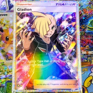 May include: A holographic Gladion Trainer card from the Pokémon Trading Card Game. The card features a character illustration with a rainbow background and text that reads "Gladion" and "Supporter". Other cards are visible in the background.