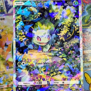 May include: A holographic Bulbasaur Pokémon trading card. The card features a green Bulbasaur character in a forest setting with the text "Vine Whip" and "HP 70". The card has a colorful, shimmering design.