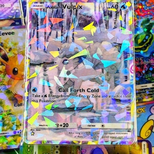 Könnte beinhalten: Eine holografische Alolan Vulpix Pokémon-Karte mit dem Text "Call Forth Cold". Die Karte hat ein farbenfrohes, geometrisches Design mit einem schneebedeckten Waldbild. Andere Pokémon-Karten umgeben sie.