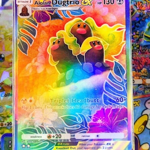 May include: A holographic Alolan Dugtrio ex Pokémon trading card. The card features three brown Dugtrio characters with yellow hair, set against a rainbow background with tropical flowers and leaves. The card text includes "Triplet Headbutt" and "HP 130".