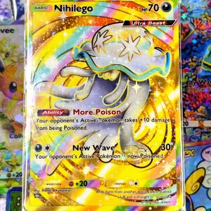 May include: A holographic Pokémon card featuring Nihilego, an Ultra Beast. The card has a gold background with rainbow accents and the text "Nihilego" at the top. The card's HP is 70. The card's abilities are "More Poison" and "New Wave".
