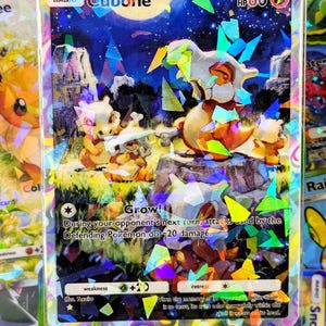 May include: A holographic Cubone Pokémon trading card. The card features a Cubone character with a bone helmet, set against a night sky background. The card has a HP of 60 and includes the text "Grow!" and other game details.