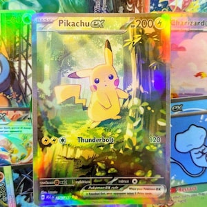 Puede incluir: Una carta coleccionable Pokémon Pikachu EX holográfica. La carta presenta un personaje Pikachu amarillo en un entorno forestal con el texto "Thunderbolt" y un nivel de poder de 120. Otras cartas son visibles en el fondo.