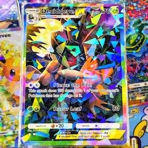 Può includere: Carta Pokémon Decidueye GX olografica. La carta presenta un'illustrazione colorata di una creatura simile a un uccello con il testo "Decidueye GX" e "HP 170". La carta include anche descrizioni degli attacchi e meccaniche di gioco.