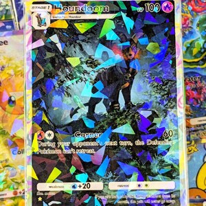 May include: A holographic Pokémon card featuring Houndoom. The card has a black and red Houndoom illustration with a forest background. The card has a HP of 100 and includes text about the card's abilities.
