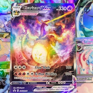 May include: A Charizard VMAX Pokémon trading card featuring a fiery dragon with a purple body and orange flames. The card has the text "Charizard VMAX" and "Gigantamax". The card's HP is 330, and it has the attacks "Claw Slash" and "G-Max Wildfire".
