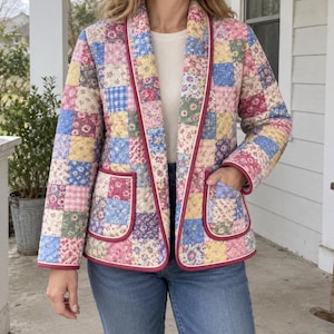 Könnte beinhalten: Eine gesteppte Jacke mit einem Patchwork-Design aus verschiedenen Blumen- und Vichy-Mustern in Rosa-, Blau-, Gelb- und Grüntönen. Die Jacke hat einen Schalkragen, lange Ärmel, zwei aufgesetzte Vordertaschen und eine dunkelrosa Paspelierung.
