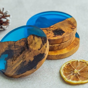 Puede incluir: Un conjunto de cuatro posavasos de madera con una parte superior de resina azul. Los posavasos tienen un patrón de vetas de madera natural. El texto "Alan and Faye Est 2024" es visible en uno de ellos.