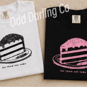 May include: Two t-shirts, one white and one black, each featuring a slice of cake graphic. The white shirt has a black and white cake design, while the black shirt has a pink cake design. The text "let them eat cake" is below the cake.