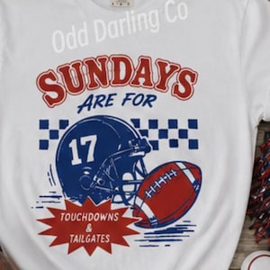 Może przedstawiać: Biały t-shirt z krótkim rękawem z grafiką zawierającą napis "SUNDAYS ARE FOR", niebieski kask do futbolu amerykańskiego z numerem "17", piłkę do futbolu oraz czerwoną gwiazdę z napisem "TOUCHDOWNS & TAILGATES" i niebieską szachownicę.