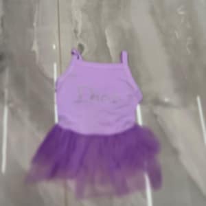 Puede incluir: Un conjunto de baile lila con una camiseta sin mangas con la palabra "Dance" en plata y una falda de tul morada en capas. Las correas son finas, adecuadas para bailar o disfrazarse.