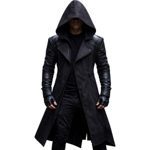 May include: A long, black hooded coat with leather sleeves and a tailored fit. The coat features a button closure and a long, flowing design. The model is wearing black gloves and black trousers. The coat is a stylish outerwear option.