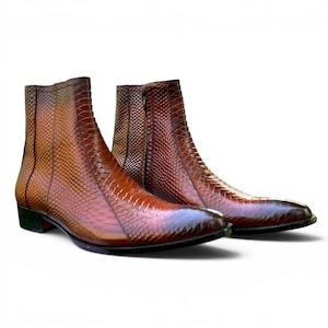Könnte beinhalten: Ein Paar braune Leder-Ankle-Boots mit einem strukturierten, schlangenlederartigen Muster. Die Stiefel haben eine spitze Zehenpartie und einen Reißverschluss an der Seite. Die Stiefel sind etwa 15 cm hoch.