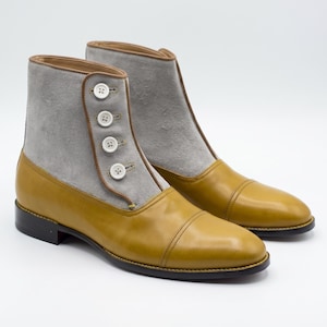 May include: A pair of two-tone ankle boots. The boots feature a mustard yellow leather toe and lower section, with a gray suede upper. They have a button closure and a brown trim. The boots are set against a white background.