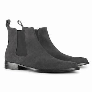 May include: A pair of charcoal grey Chelsea boots. The suede boots have elastic side panels and a pull tab. They feature a low heel and a minimalist design. The boots are a versatile footwear choice.