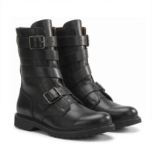 Peut inclure: Une paire de bottes noires mi-mollet avec une finition lisse, un bout arrondi et une semelle épaisse crantée. Chaque botte est fixée par deux brides réglables sur la tige et une bride sur l'empeigne, dotées de boucles en métal argenté.