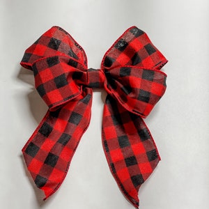 May include: A large, decorative bow featuring a classic red and black buffalo plaid pattern. The bow is made of a sheer fabric, with long, flowing tails. Perfect for holiday decor or gift wrapping.