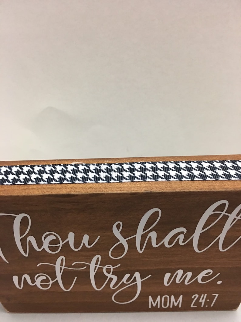 May include: Wooden block with the phrase "Thou shalt not try me" in white script. A black and white houndstooth ribbon trims the top edge. The text "MOM 24:7" is below the main text.