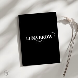 Peut inclure: Une enseigne rectangulaire noire avec le texte blanc LUNA BROW STUDIO dans une police serif grasse, et les mots BROW BAR courbés en un petit arc au-dessus du côté droit du texte. L'enseigne est placée à côté d'une tige de plante séchée.