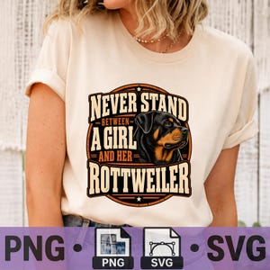 May include: A cream-colored t-shirt featuring a graphic print of a Rottweiler dog head. The text reads: NEVER STAND BETWEEN A GIRL AND HER ROTTWEILER. The design is enclosed in a circular border with orange and black tones, centered on the chest.