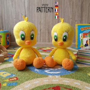 May include: Two handmade yellow crochet bird dolls with orange feet and beaks, and green eyes. The dolls are sitting on a colorful rug, with children's books and toys in the background. The text "PDF PATTERN" is visible.