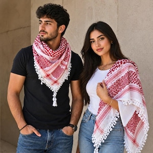 Puede incluir: Un pañuelo keffiyeh rojo y blanco con un patrón geométrico tradicional y borlas blancas en los bordes. El pañuelo se lleva drapeado alrededor del cuello y los hombros, mostrando la textura del tejido y el distintivo esquema de colores rojo y blanco.