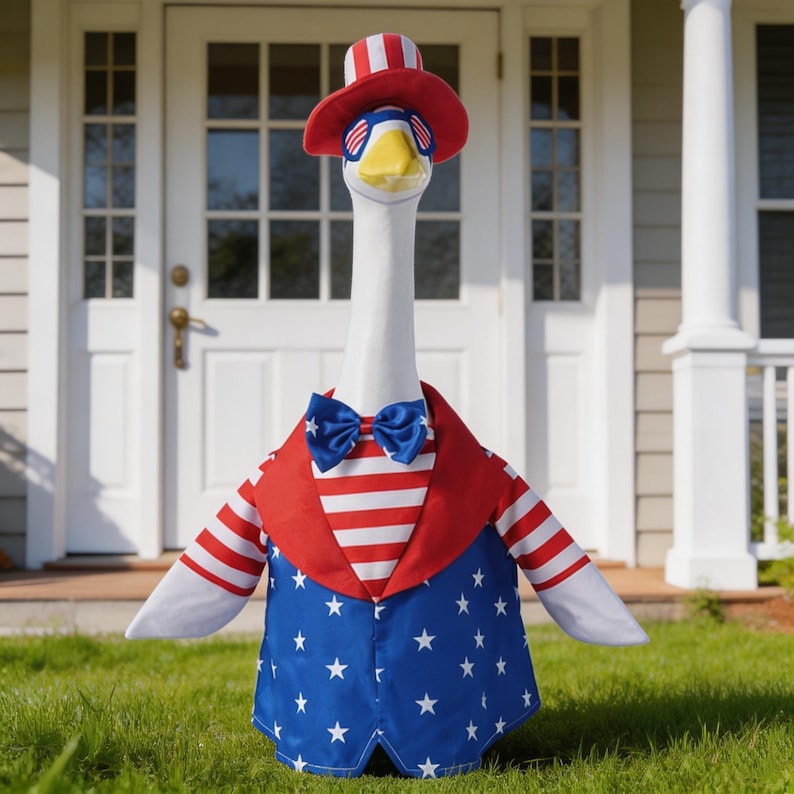 May include: A decorative goose statue dressed in patriotic attire. The goose wears a red, white, and blue outfit, including a jacket with stars and stripes, a bow tie, and a hat. The goose is standing on green grass in front of a white door.