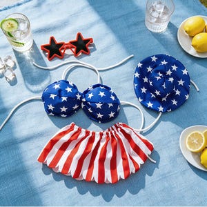 May include: A patriotic-themed bikini set with a blue top and hat, both adorned with white stars. The set includes a red and white striped skirt. Star-shaped sunglasses and lemons complete the summer ensemble.