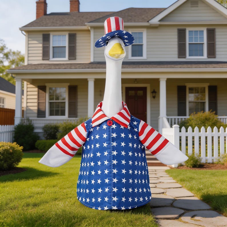 May include: A white goose wearing a patriotic outfit, including a blue jacket with white stars, a red and white striped collar, and a matching top hat. The goose stands on a green lawn in front of a house.