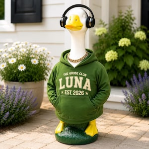 May include: A white goose statue wearing black over-ear headphones, a gold chain necklace, and a green hooded sweatshirt with the text THE GOOSE CLUB LUNA EST. 2026 printed in cream. The goose has a yellow beak and yellow feet on a green base.